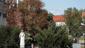 A statue in a garden with a brick wall and a building with a dome in the background.