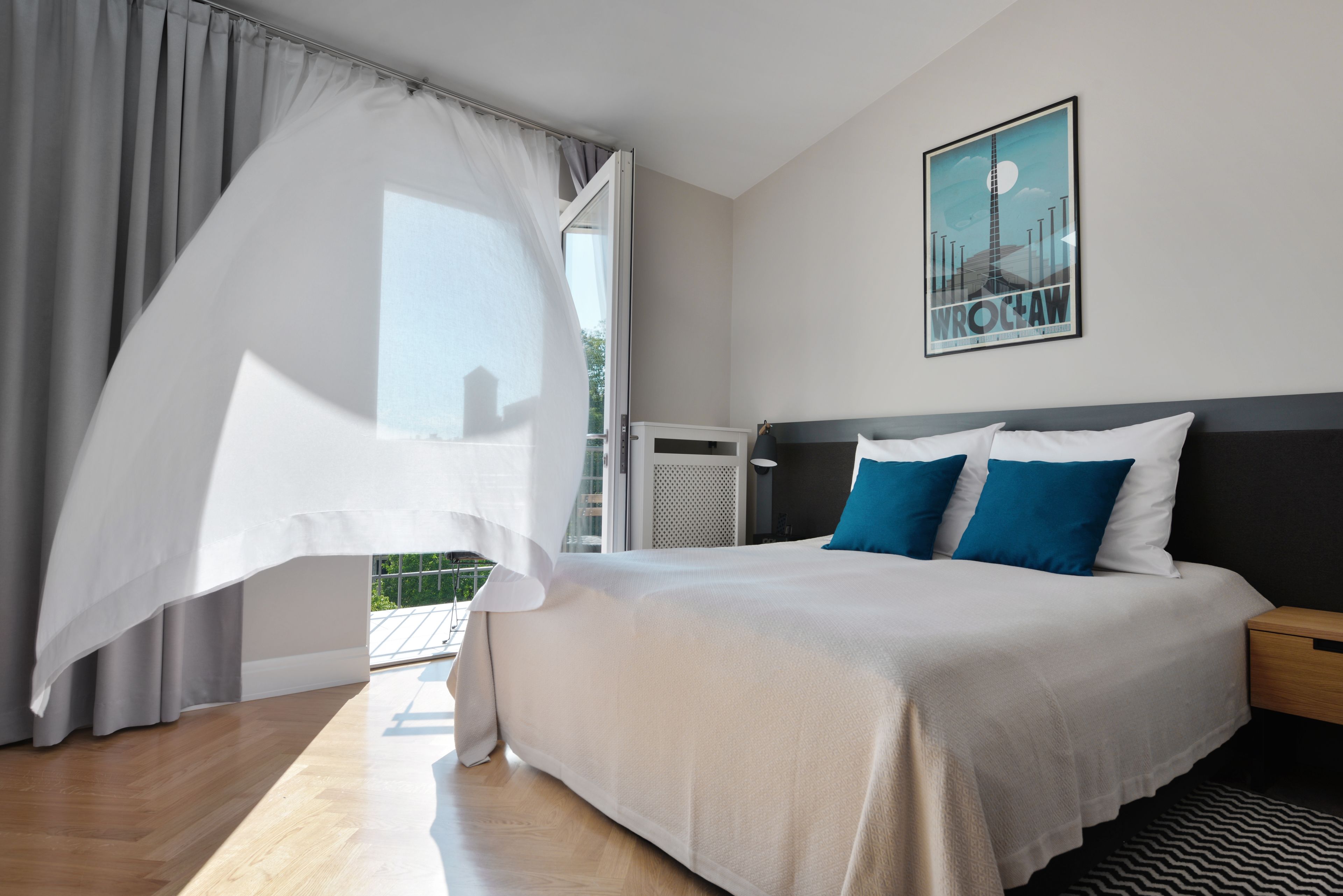 Une chambre d’hôtel moderne avec un grand lit, un balcon doté d’un auvent blanc et une affiche accrochée au mur.