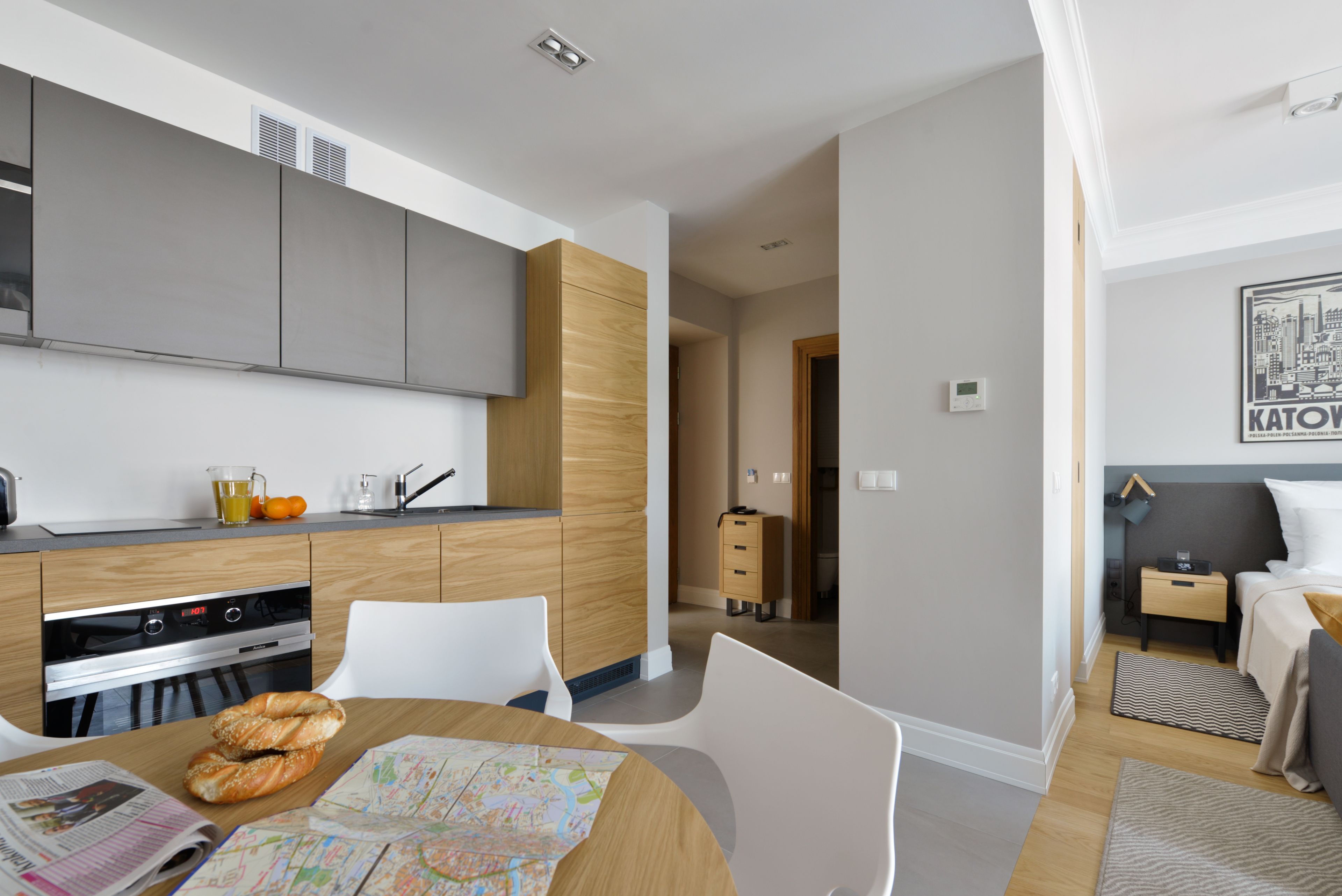 A modern kitchen with built-in appliances, a dining area with a map, and a bedroom with a bed and nightstand.