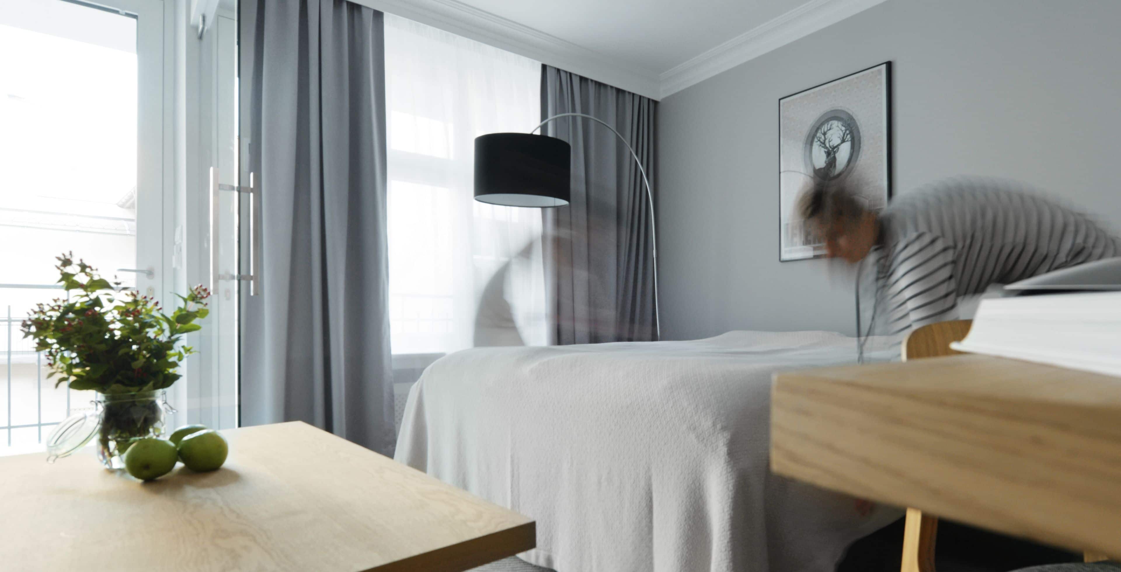 Una habitación de hotel con una cama, una mesita de noche con un florero, una lámpara y un cuadro en la pared.