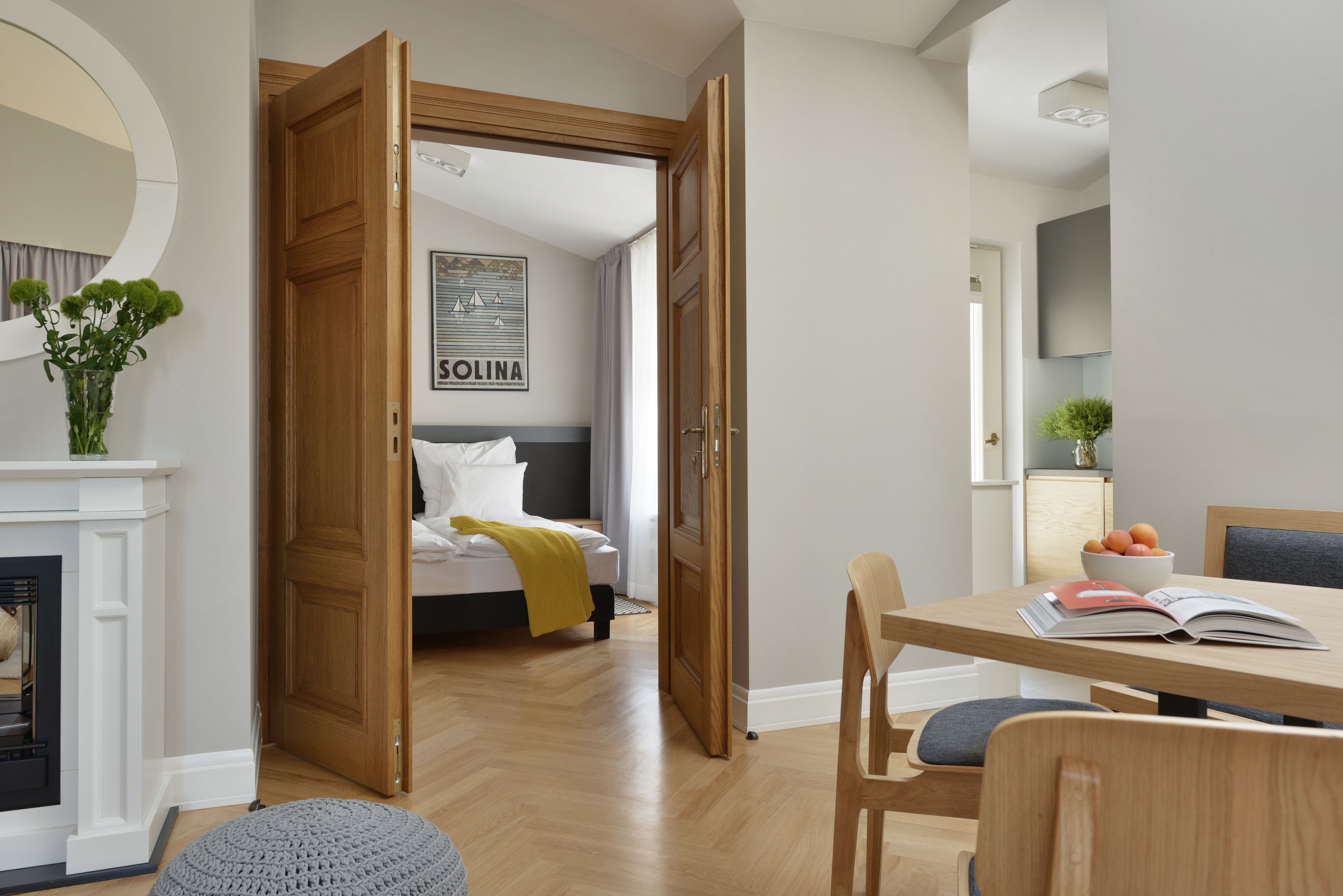Una habitación de hotel moderna con una puerta de madera, una cama con un plaid amarillo, un área de comedor con una mesa y sillas, y una chimenea.