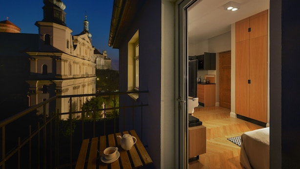 Un balcón con vistas a un edificio histórico, una mesa de madera con tetera y taza, e interiores modernos con armarios de madera y una cama.
