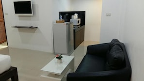 Una sala de estar moderna con un sofá negro, una pequeña mesa de centro blanca y un televisor de pantalla plana montado en la pared.
