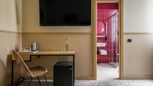 Hotellihuone, jossa on työpöytä, tuoli, televisio ja pieni musta jääkaappi.
