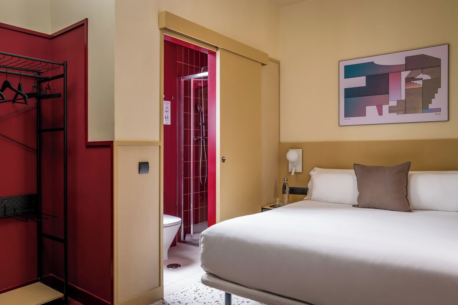Une chambre d’hôtel avec un lit, une table de chevet, une porte rouge et une douche.