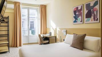 Une chambre d’hôtel avec un lit, un bureau, une chaise, une télévision et une fenêtre avec des rideaux.