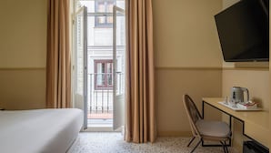 Hotellihuone, jossa on sänky, työpöytä tuolilla, televisio ja näkymä ulos parvekkeelle.