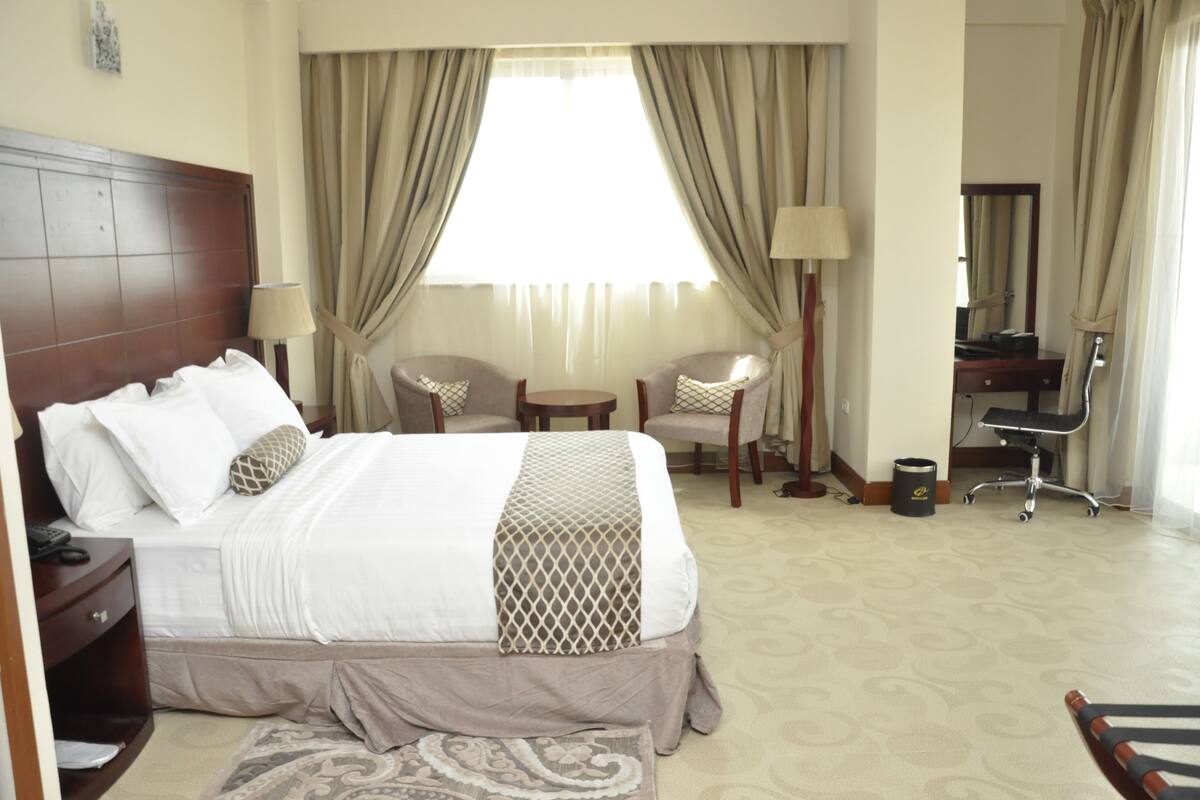 A hotel room with a bed, bedside table, lamp, chair, desk, and mirror.