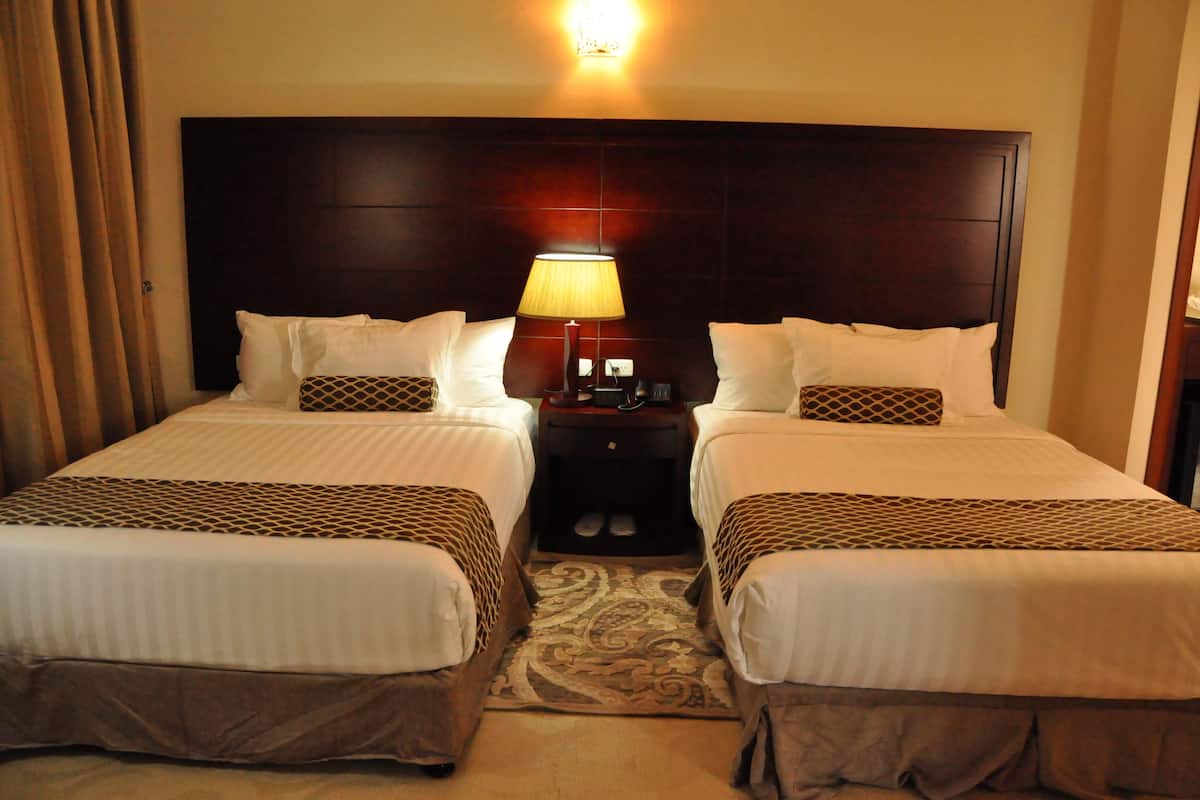 A hotel room with two beds, a nightstand with a lamp, and a patterned rug.