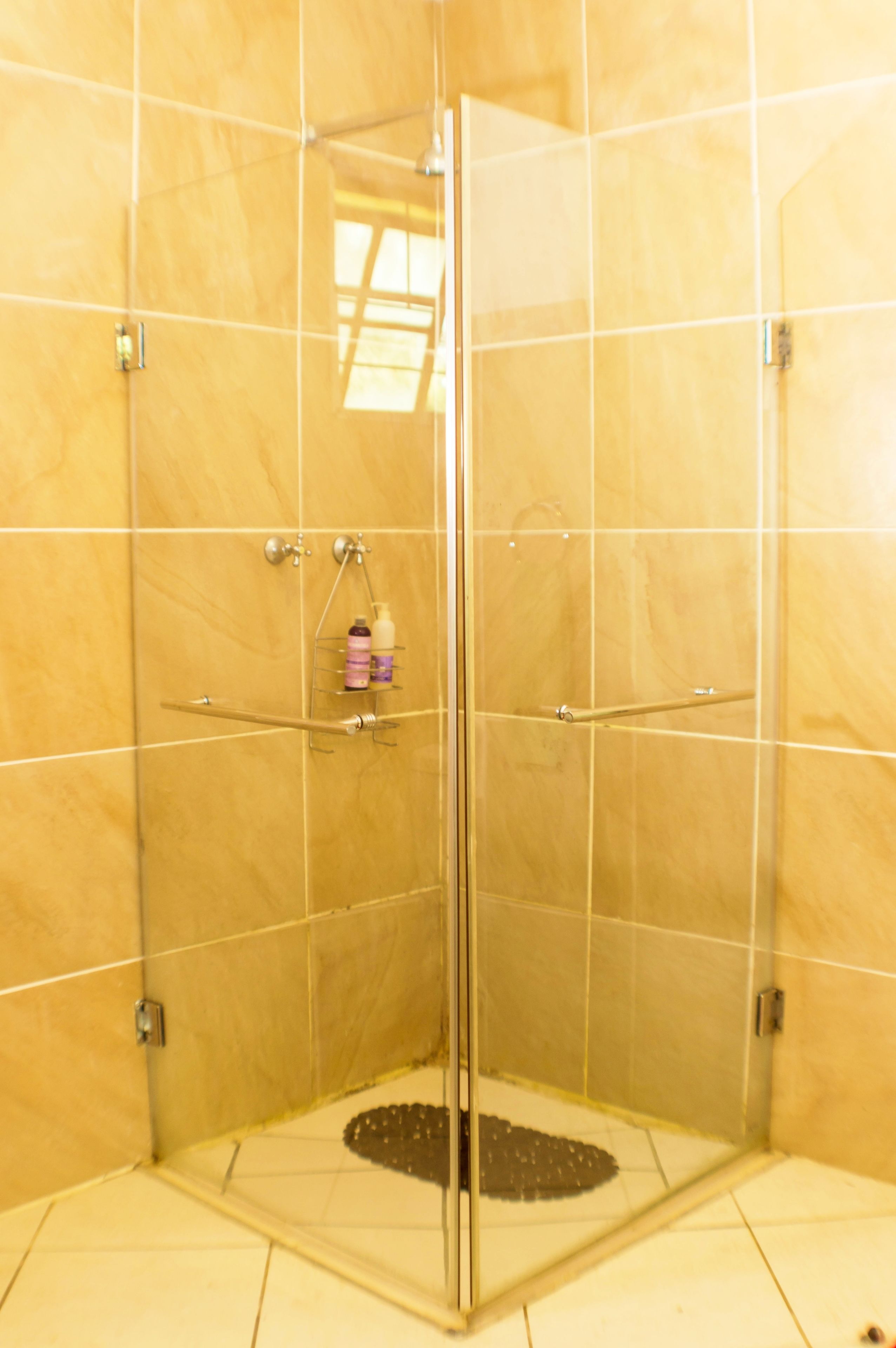 Un área de ducha con paredes de vidrio, suelo de azulejos y un pequeño estante con artículos de aseo.