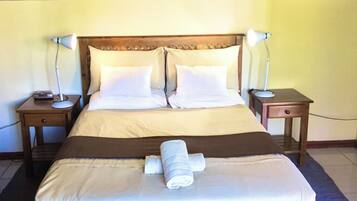 A neatly made bed with white linens, two bedside tables with lamps, a painting on the wall, and a wooden table with a book in the foreground.