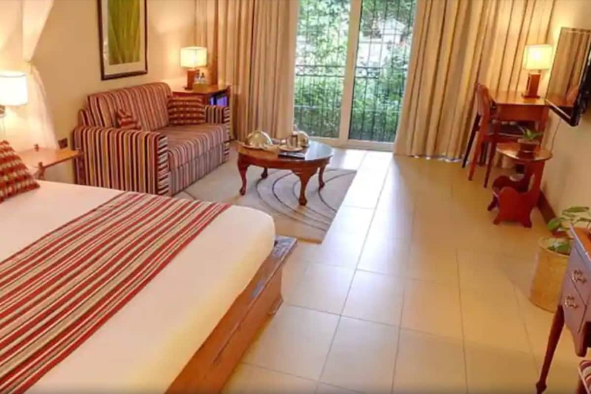 A hotel room with a large bed, a sofa, a dining table, and a view of the outdoors.