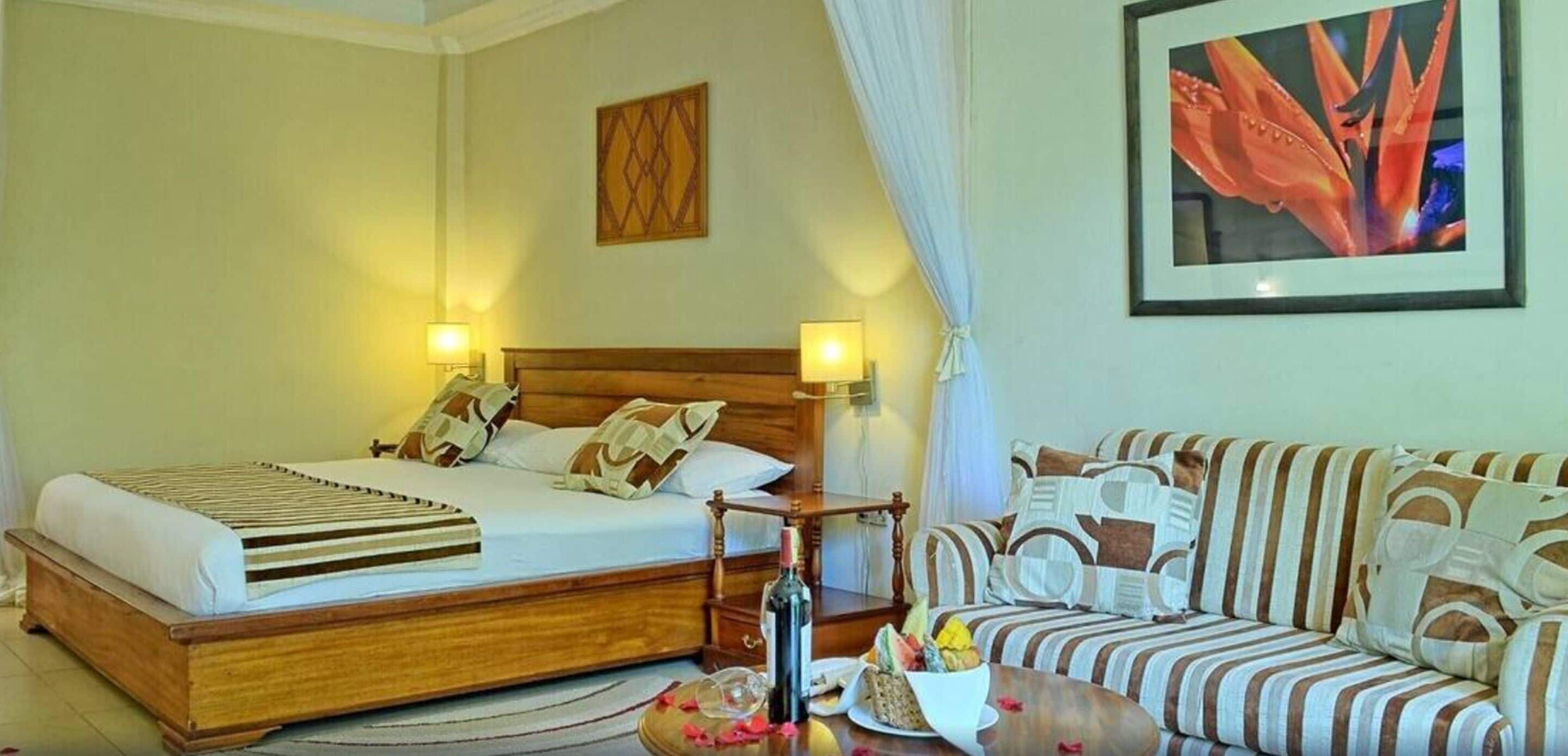 Ein Hotelzimmer mit einem hölzernen Bett, einem gestreiften Sofa, einem Gemälde und einem Tisch mit Obstkorb.