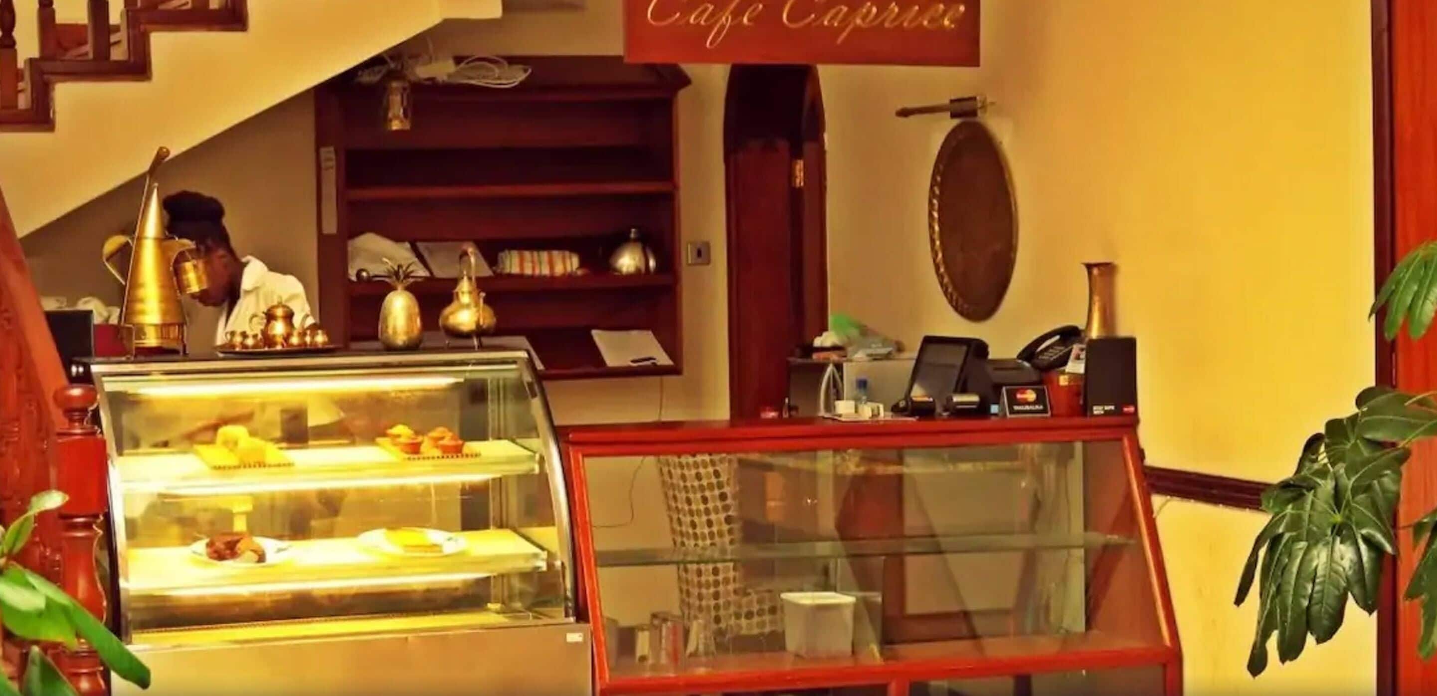 Un café avec une vitrine remplie de pâtisseries, une caisse enregistreuse et une enseigne au-dessus indiquant « Café Caprice ».