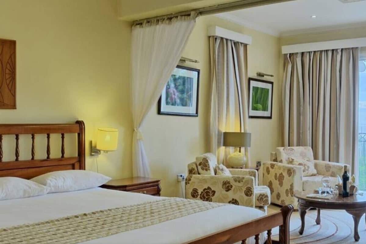 A hotel room with a large bed, a sitting area with floral armchairs, a small table, and a balcony with a view.