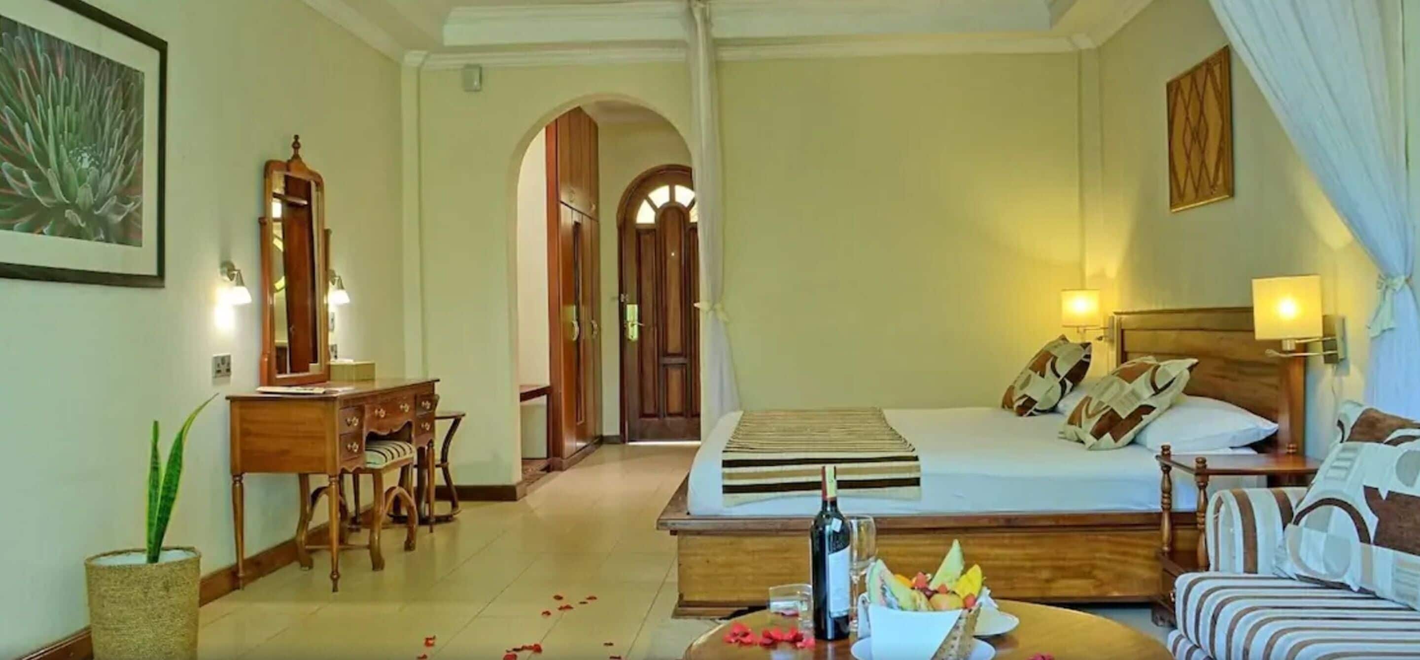 A hotel room with a bed, a desk, a chair, and a sofa. There is a mirror, a lamp, and a picture on the wall.