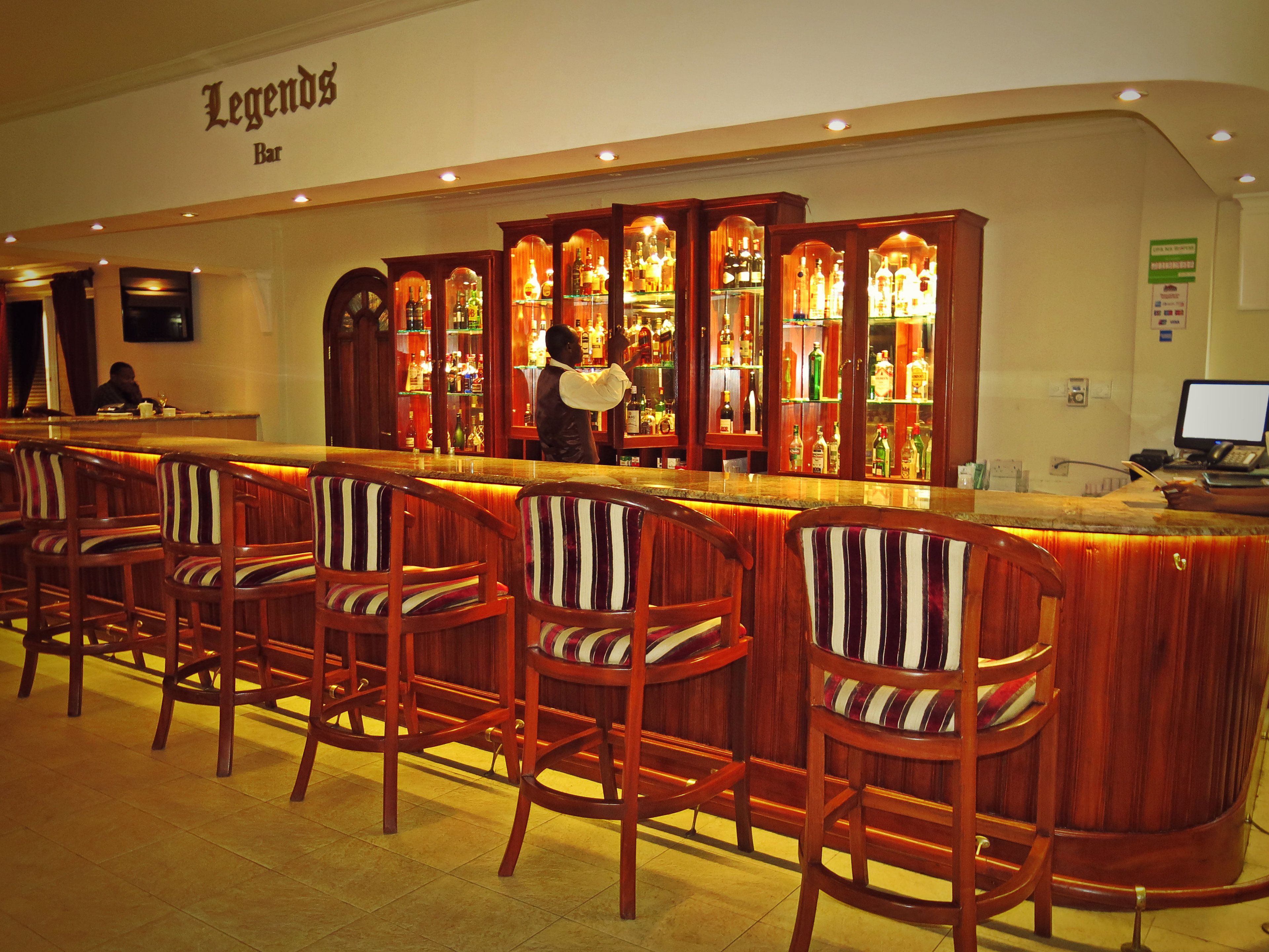 A bar area with a wooden bar counter, striped cushioned bar stools, and a bartender.