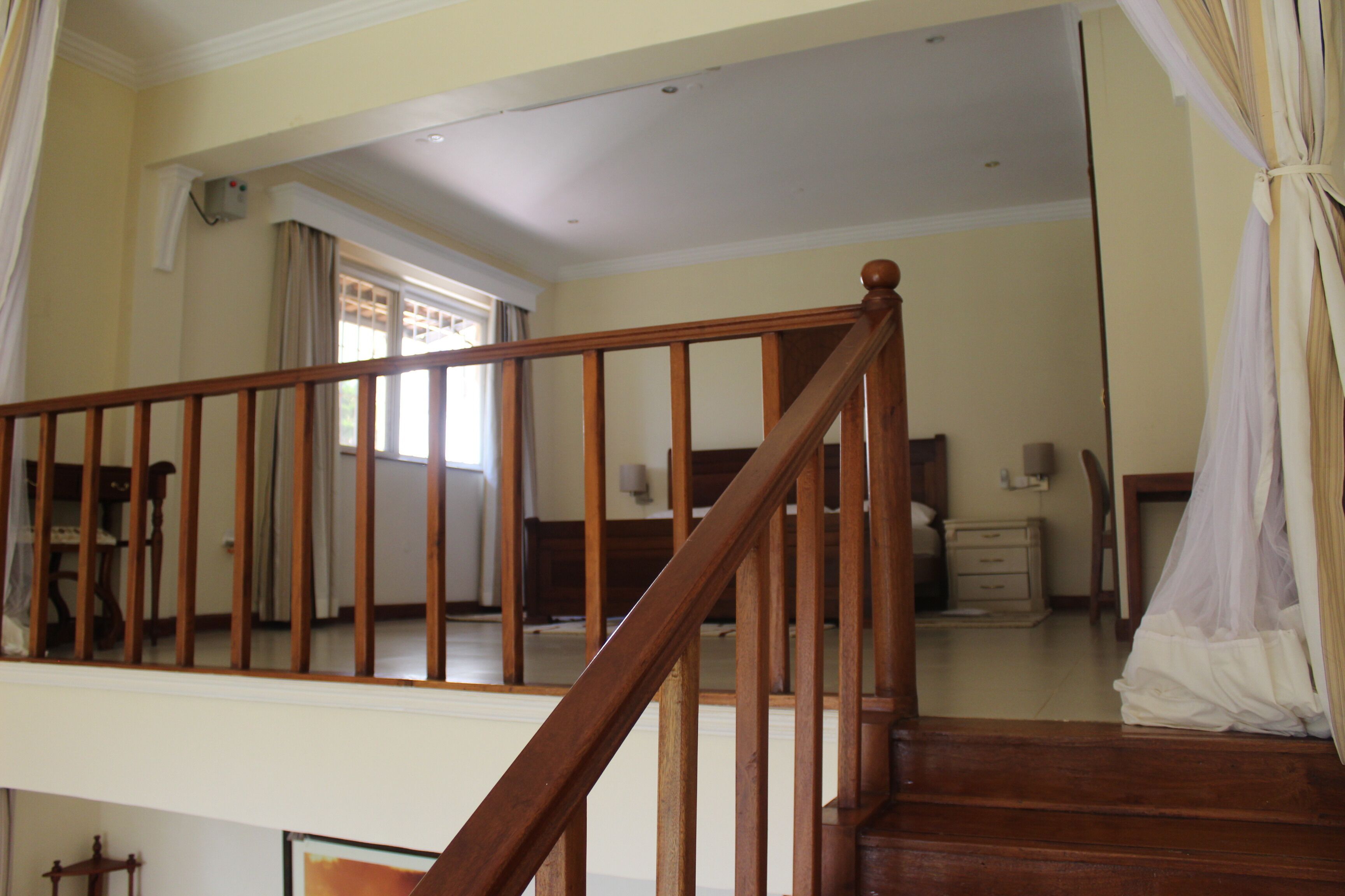 Um quarto espaçoso com escada de madeira, uma cama, mesa de cabeceira e janela com cortinas.