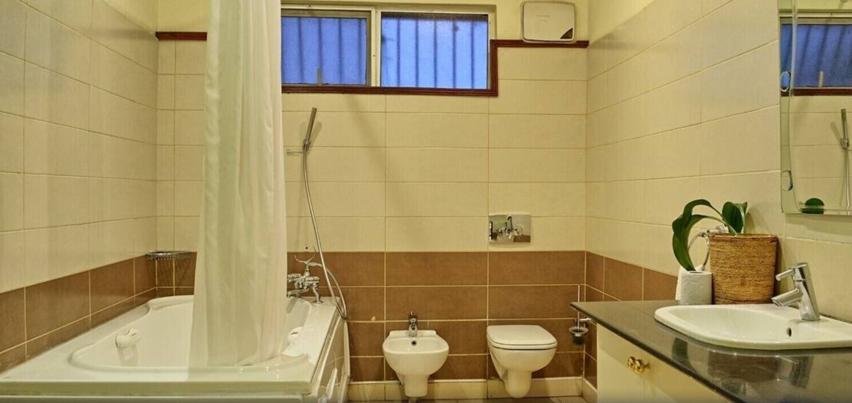 Ein Badezimmer mit einer Badewanne, einem Bidet, einer Toilette, einem Waschbecken und einem Fenster mit Vorhängen.