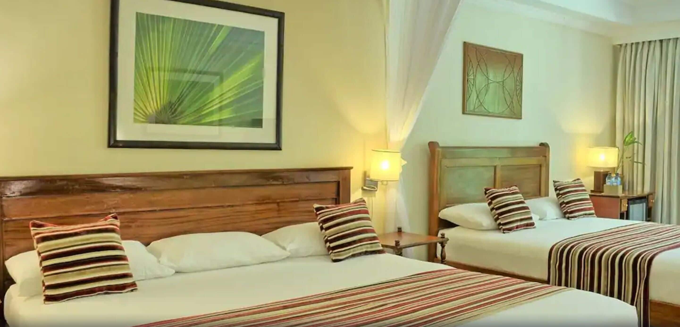 A hotel room with two beds, each with striped bedding and pillows, a wooden headboard, wall art, and bedside lamps.