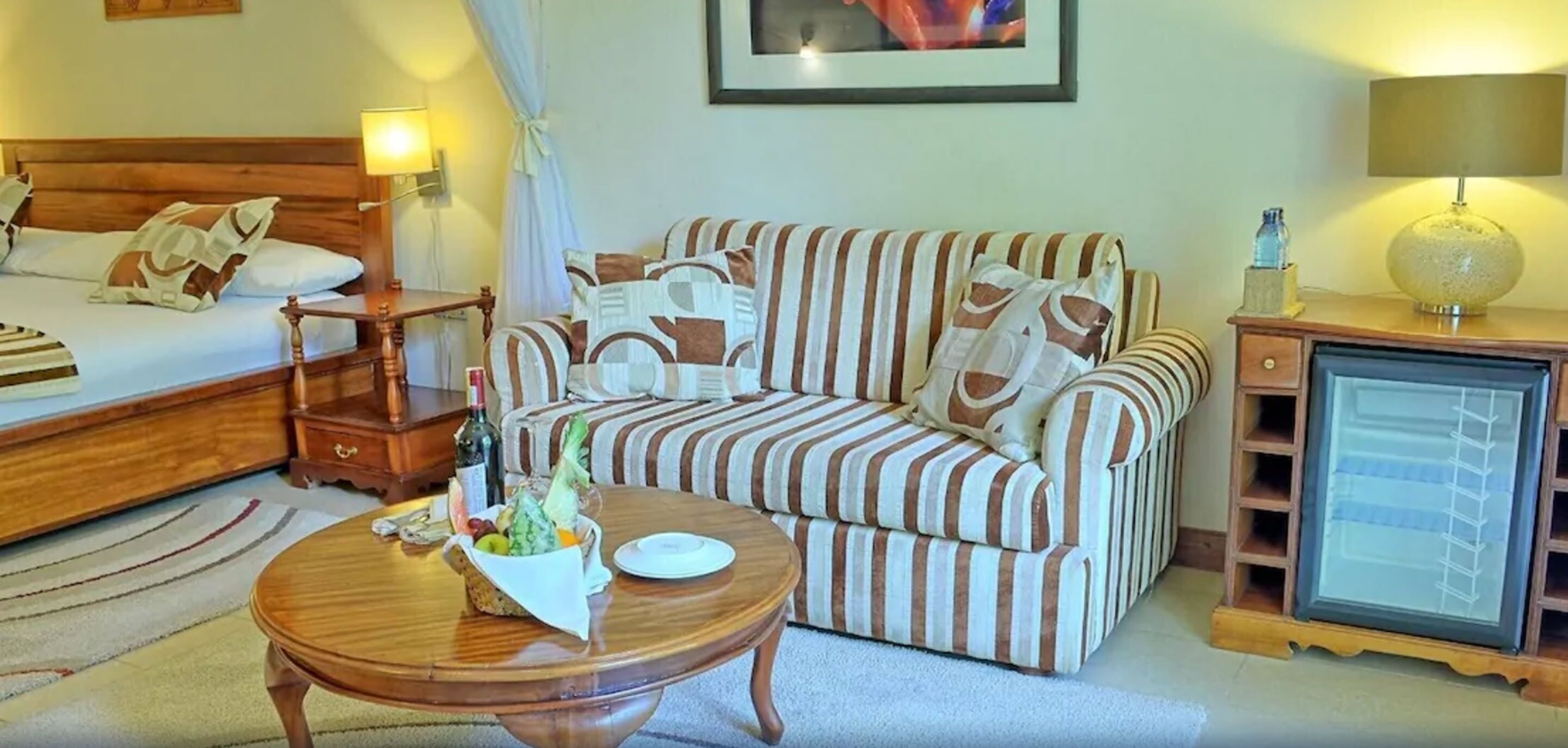 A hotel room with a bed, a sofa, a small table with fruit, a lamp, and a TV.