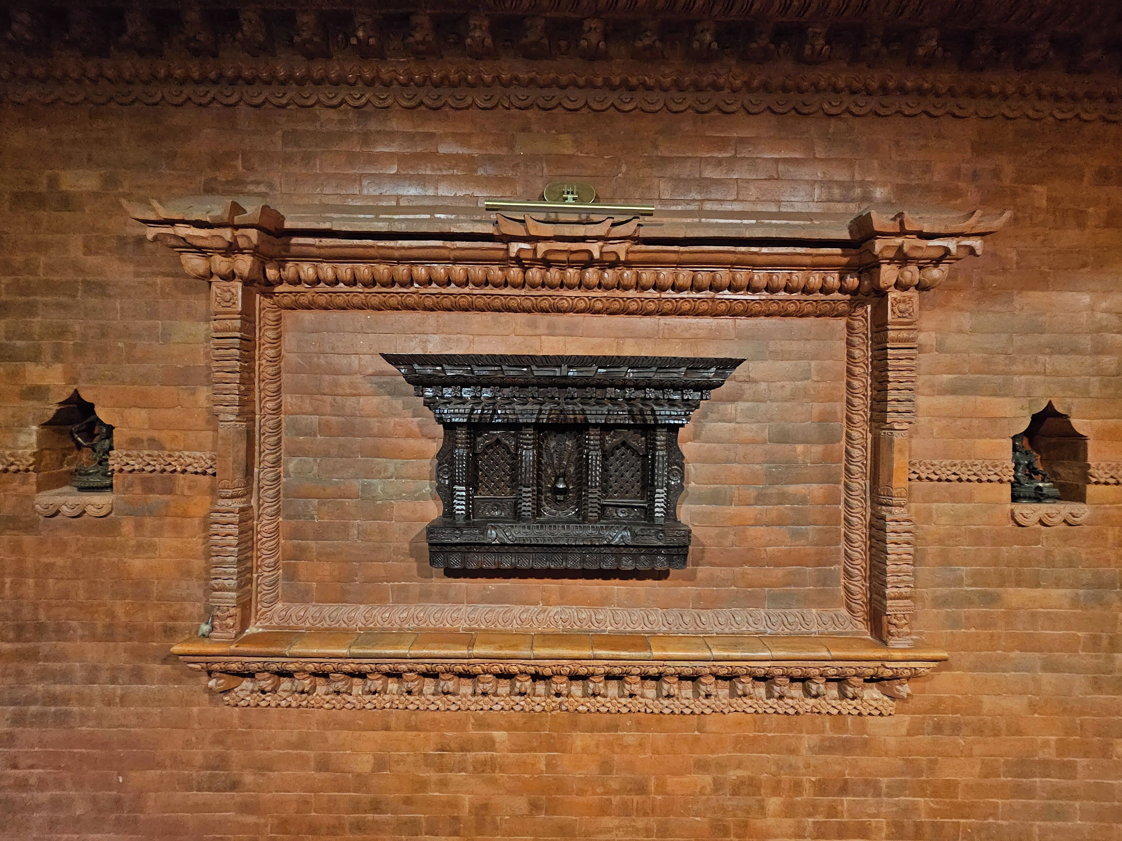 A detailed stone fireplace with intricate carvings and a traditional design, set within a brick wall.