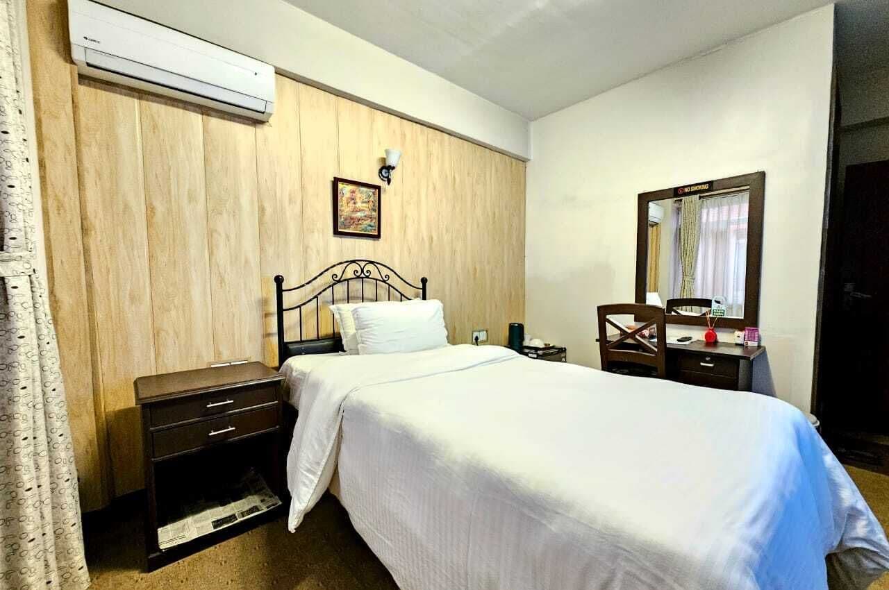 A hotel room with a bed, a nightstand, a dresser, a mirror, and an air conditioning unit on the wall.