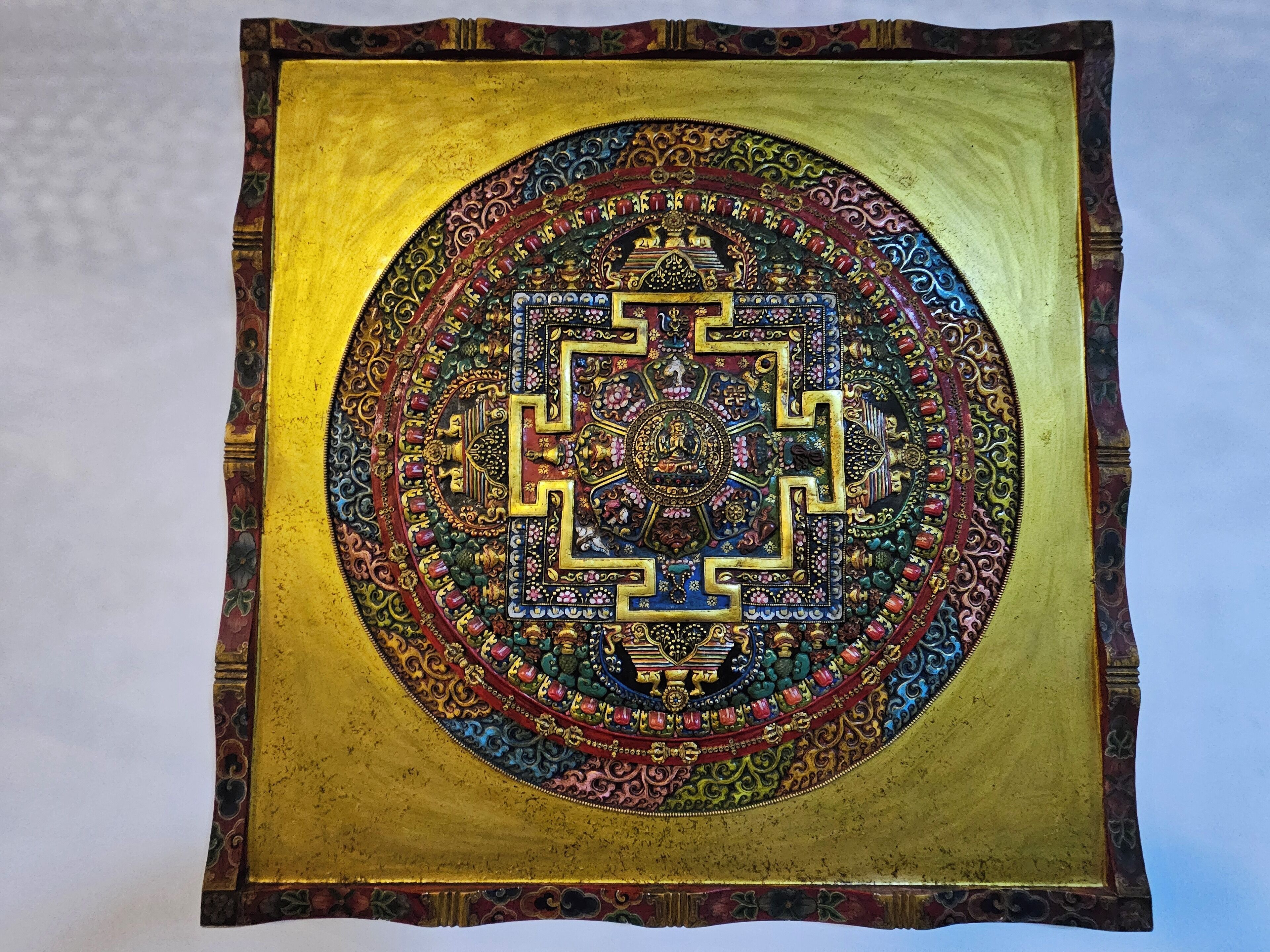 Un objeto cuadrado con un diseño circular central rodeado de patrones intrincados y un borde dorado.