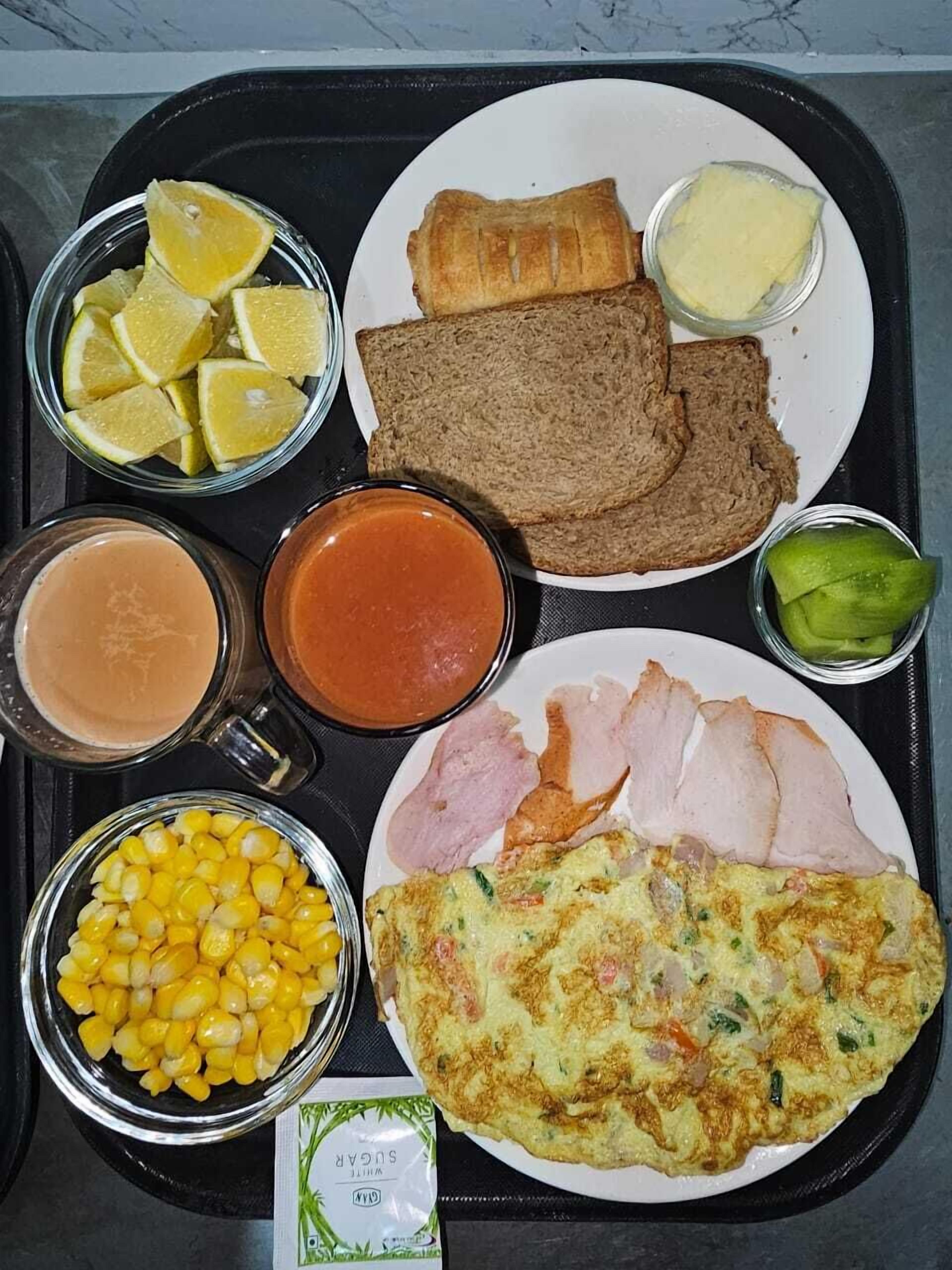 A tray with various food items including bread, ham, corn, and a plate with an omelette.