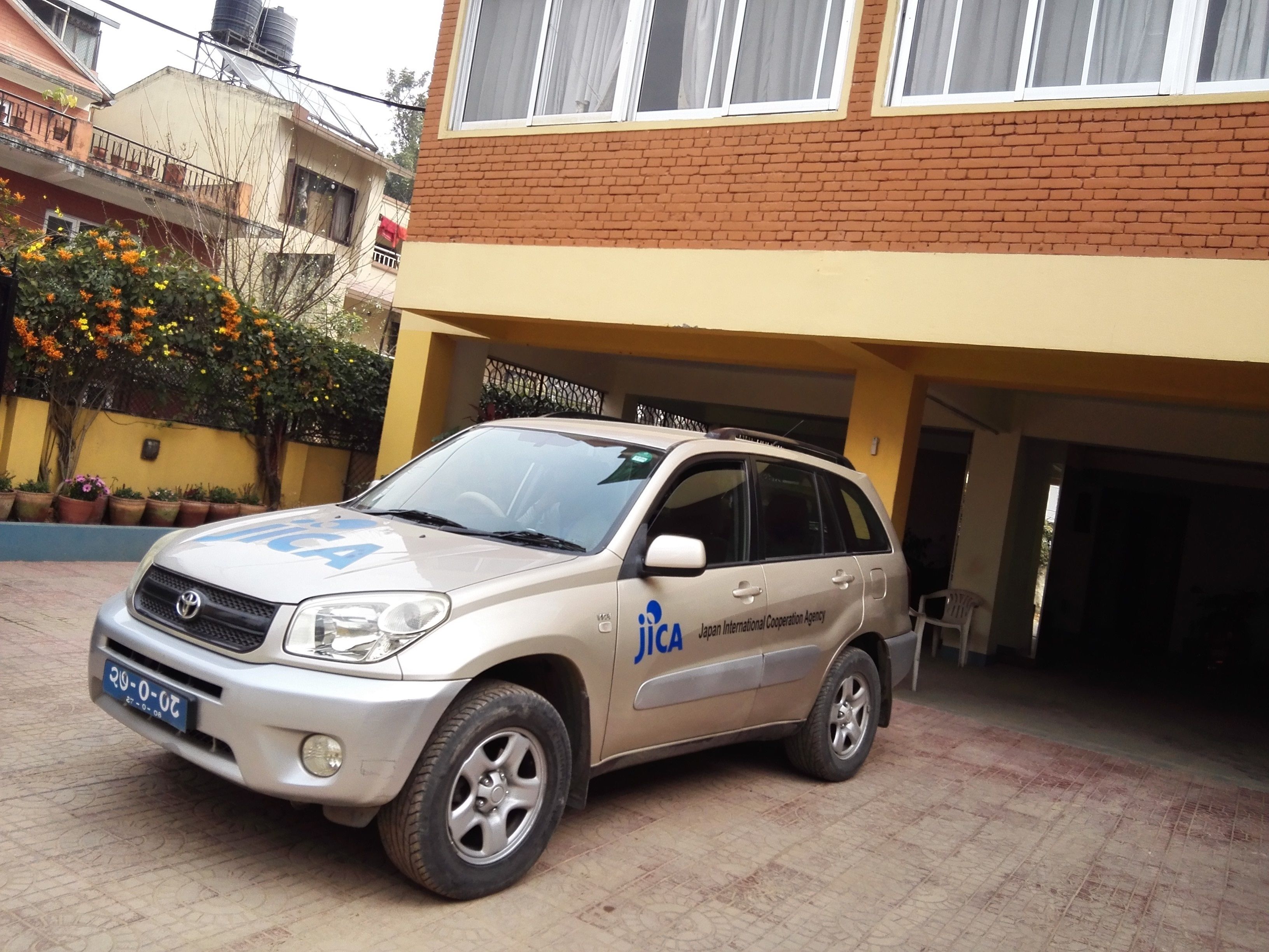 Un SUV plateado estacionado frente a un edificio con un letrero que dice “Japan International Cooperation Agency.”