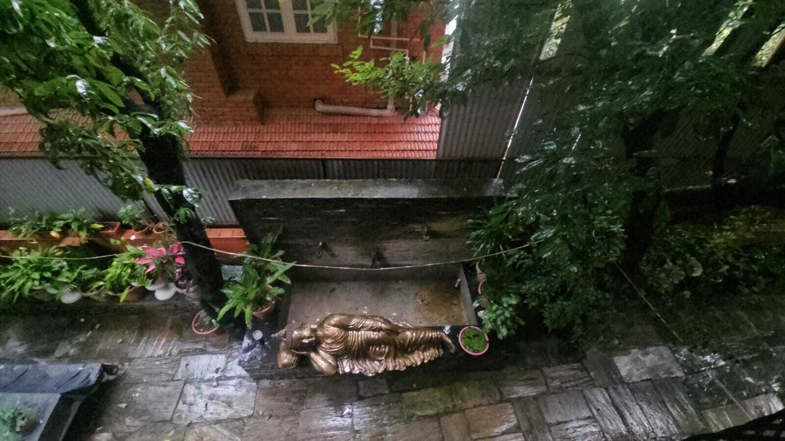 A wet stone pathway leading to a wooden bench with a decorative metal sculpture.
