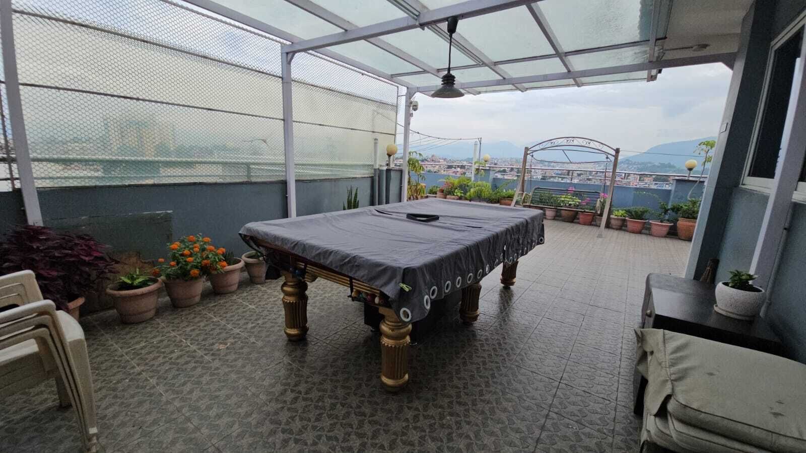 A covered patio area with a table and chairs, surrounded by potted plants and a view of the cityscape.