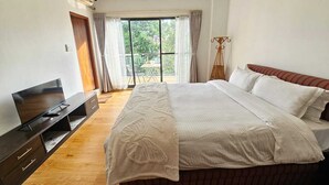 Un dormitorio con una cama grande, un televisor sobre un mueble de madera y una ventana con cortinas.