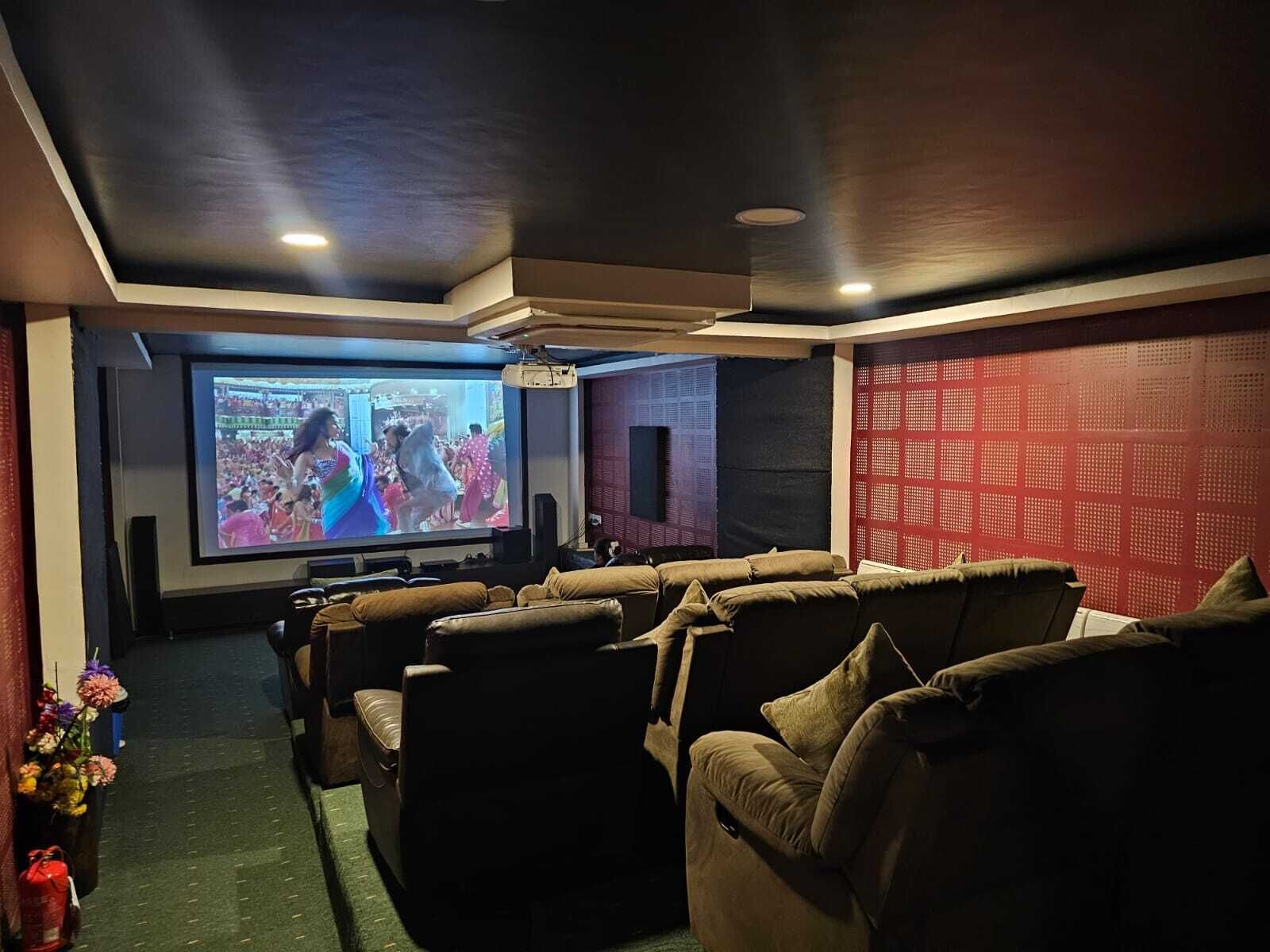 A home theater room with a large screen, multiple seating areas, and a red patterned wall.