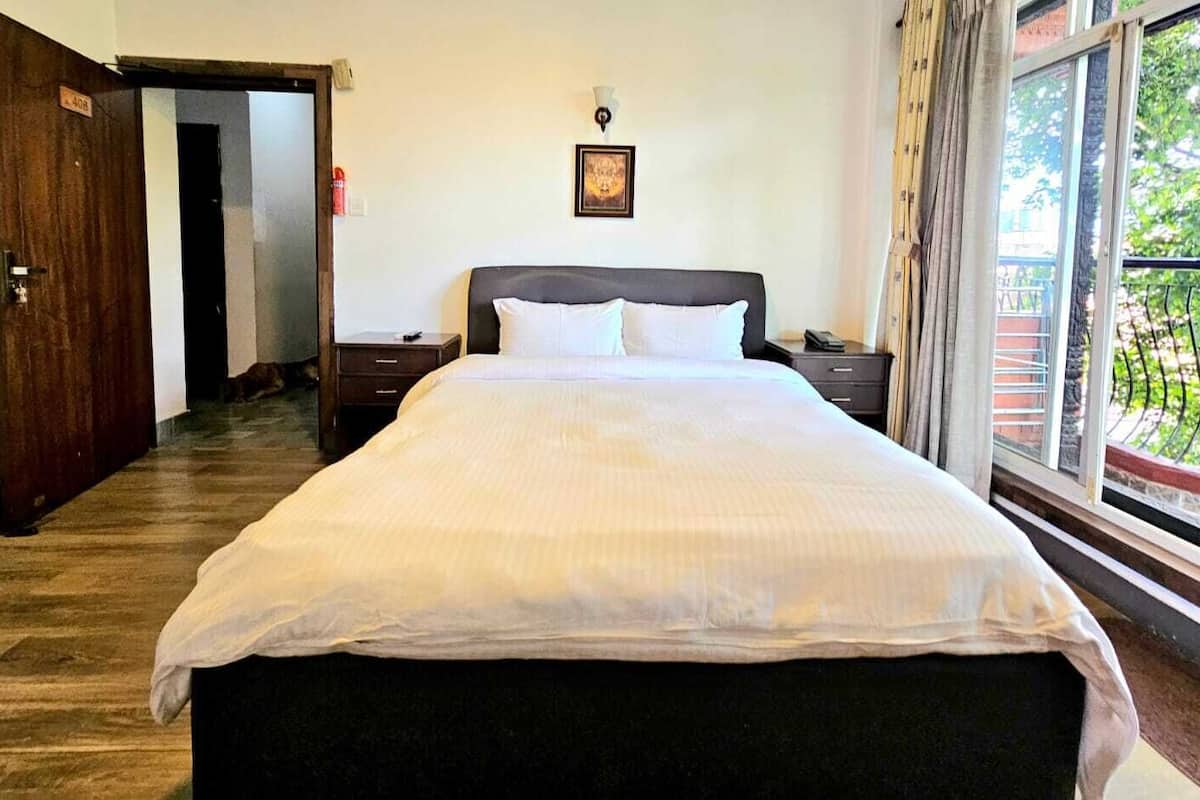 Une chambre d’hôtel avec un grand lit, une table de chevet, une commode, une fenêtre donnant sur un beau paysage et une porte.