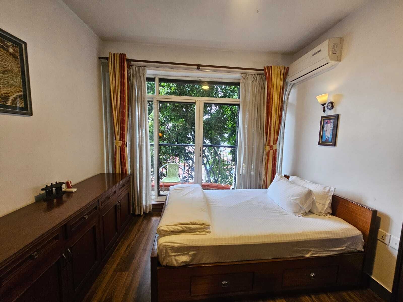 Un dormitorio con cama, cómoda, ventana con cortinas y aire acondicionado instalado en la pared.