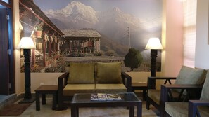 A cozy living room with a sofa, armchairs, and a coffee table. A large mural of a mountain landscape is on the wall behind the seating area. - Sagarmatha Apartment Bed & Breakfast (Lalitpur)