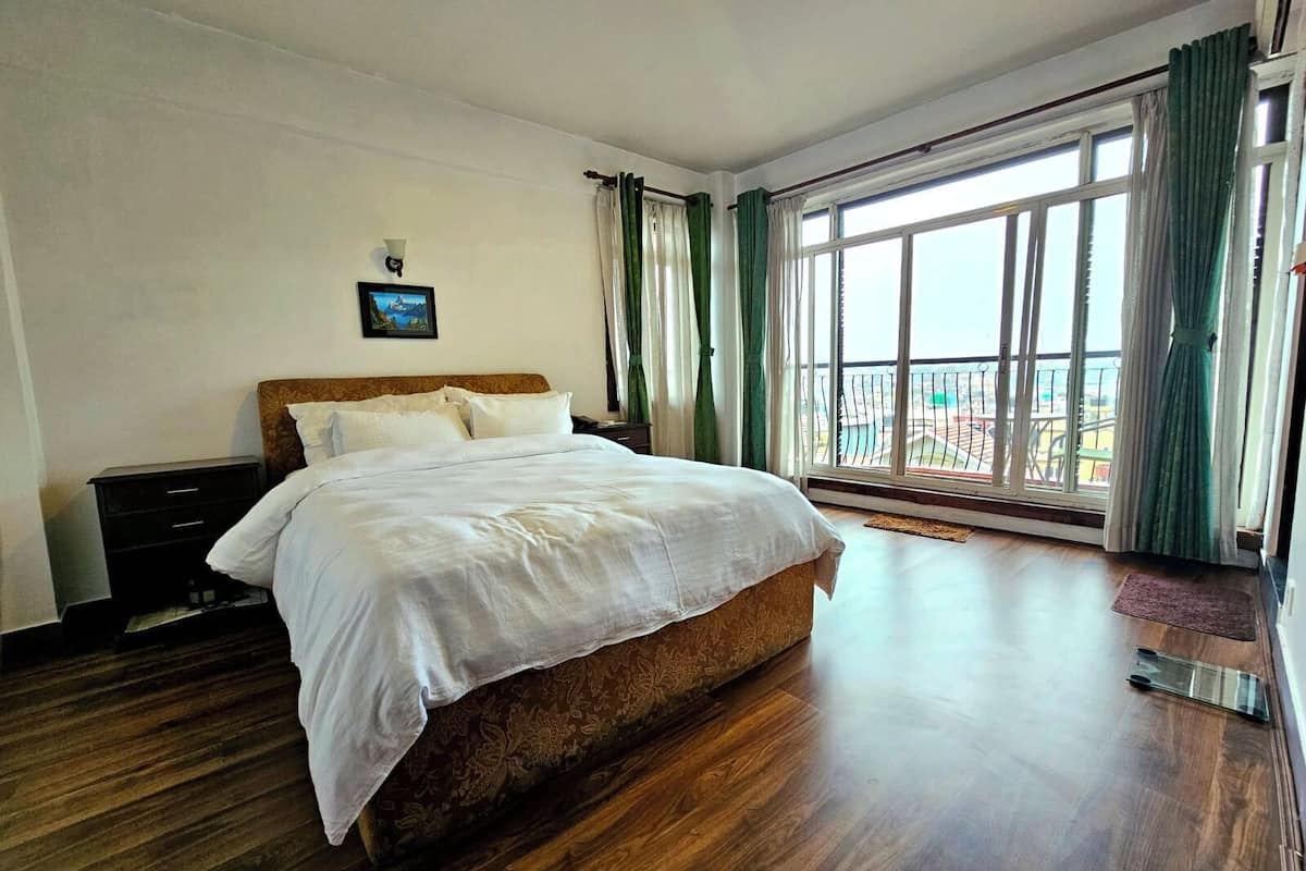 Une chambre spacieuse avec un grand lit, un plancher en bois, une table de chevet et une vue sur un balcon grâce à de grandes fenêtres.