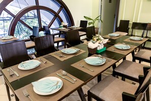 Un espace repas avec une longue table dressée pour accueillir plusieurs convives, des chaises et une grande fenêtre offrant une belle vue.