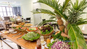 Une table de buffet proposant une variété d’aliments et de boissons, notamment des salades, des fruits et des boissons diverses.