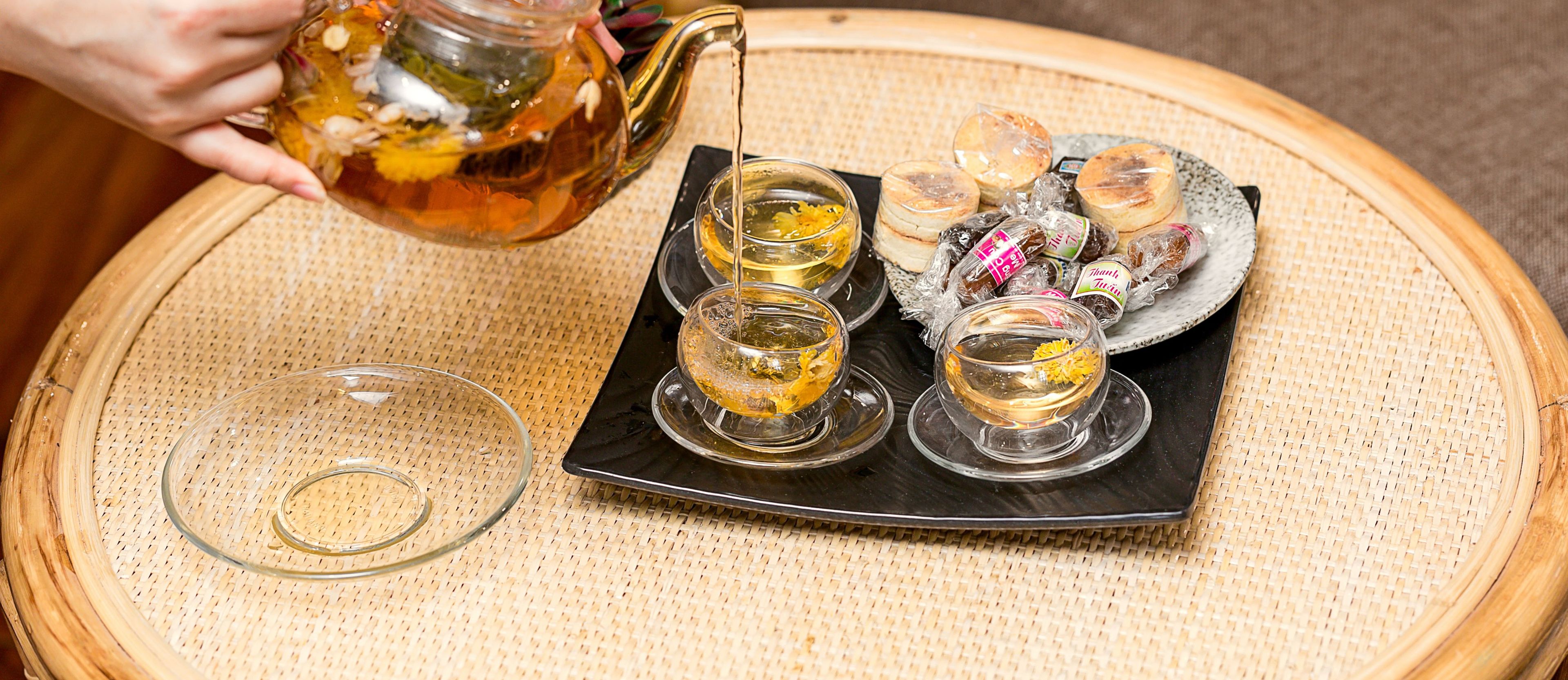 Un plateau avec quatre tasses à thé en verre, une assiette de pâtisseries et une théière posée sur un tapis tissé.