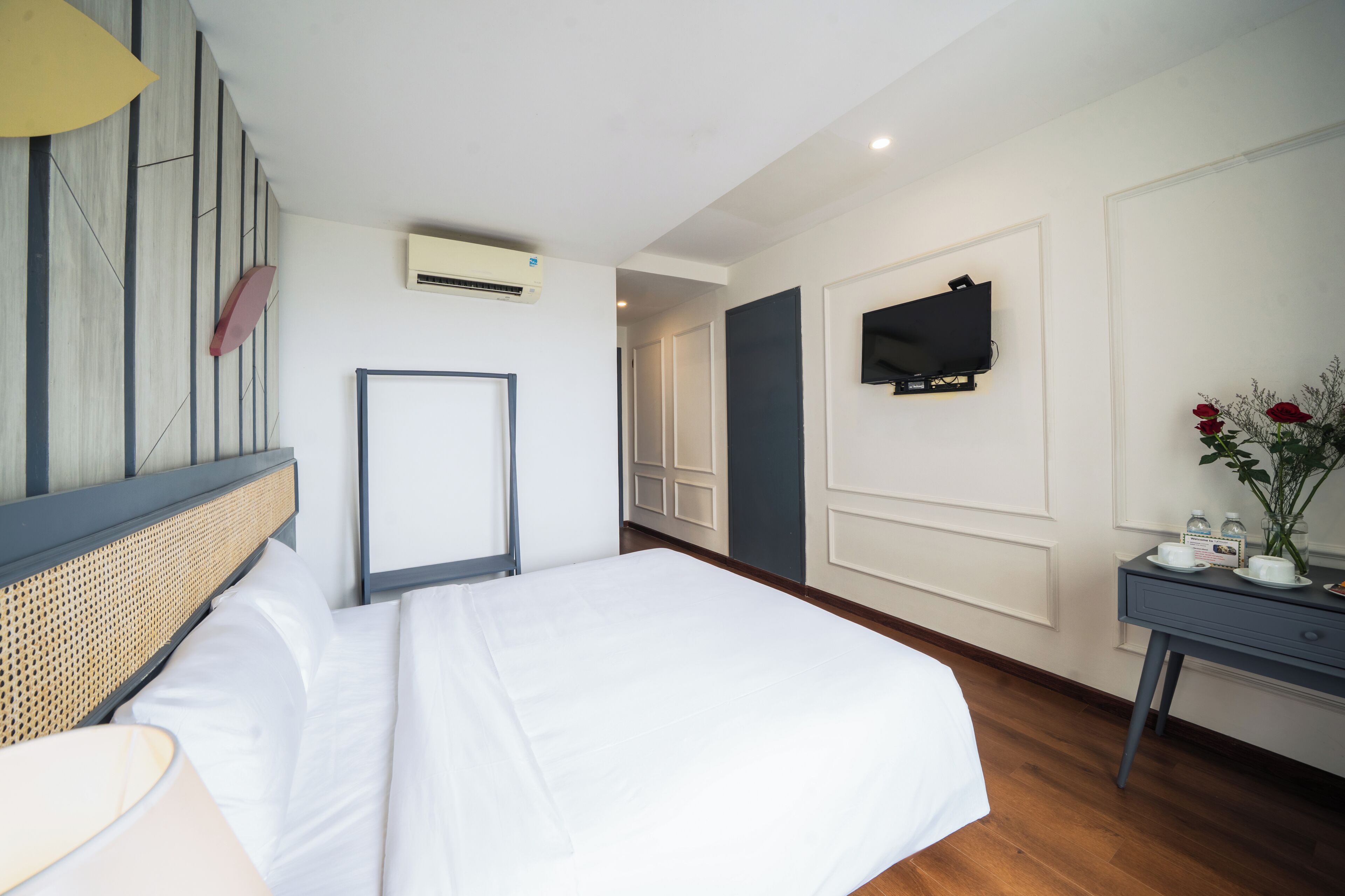 A hotel room with a bed, a bedside table, a TV mounted on the wall, and an air conditioning unit.