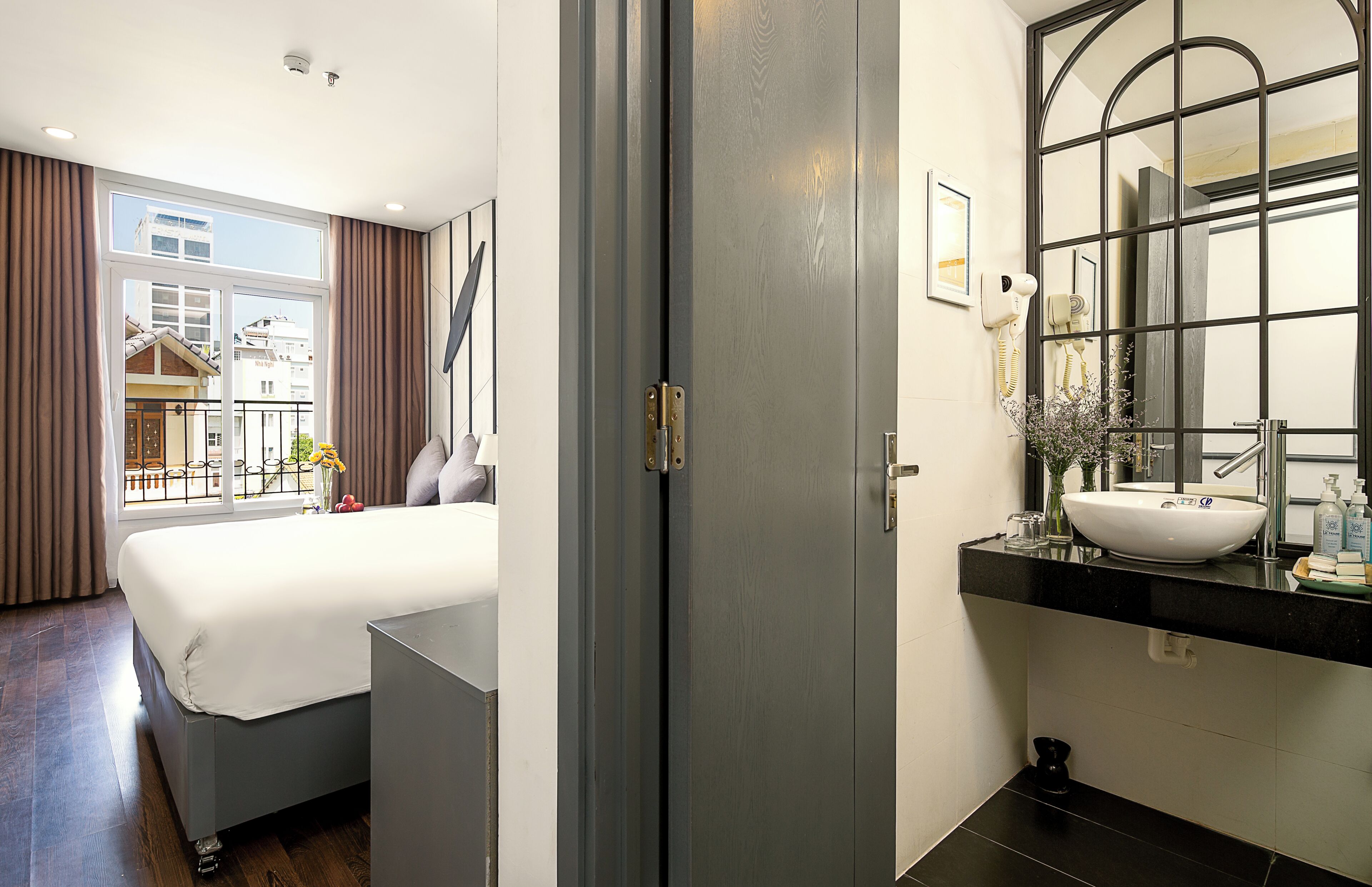 A hotel room with a large bed, a bathroom with a modern sink and mirror, and a view of the outside through the window.