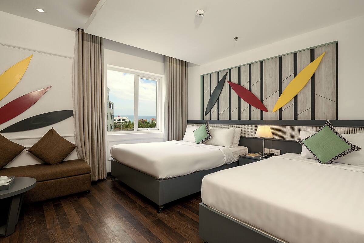 Une chambre d’hôtel avec deux lits, un canapé, une table de chevet et une fenêtre avec des rideaux.