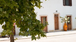 Vista de la calle con un edificio blanco que tiene tres puertas de madera y un jarrón naranja grande en la acera.