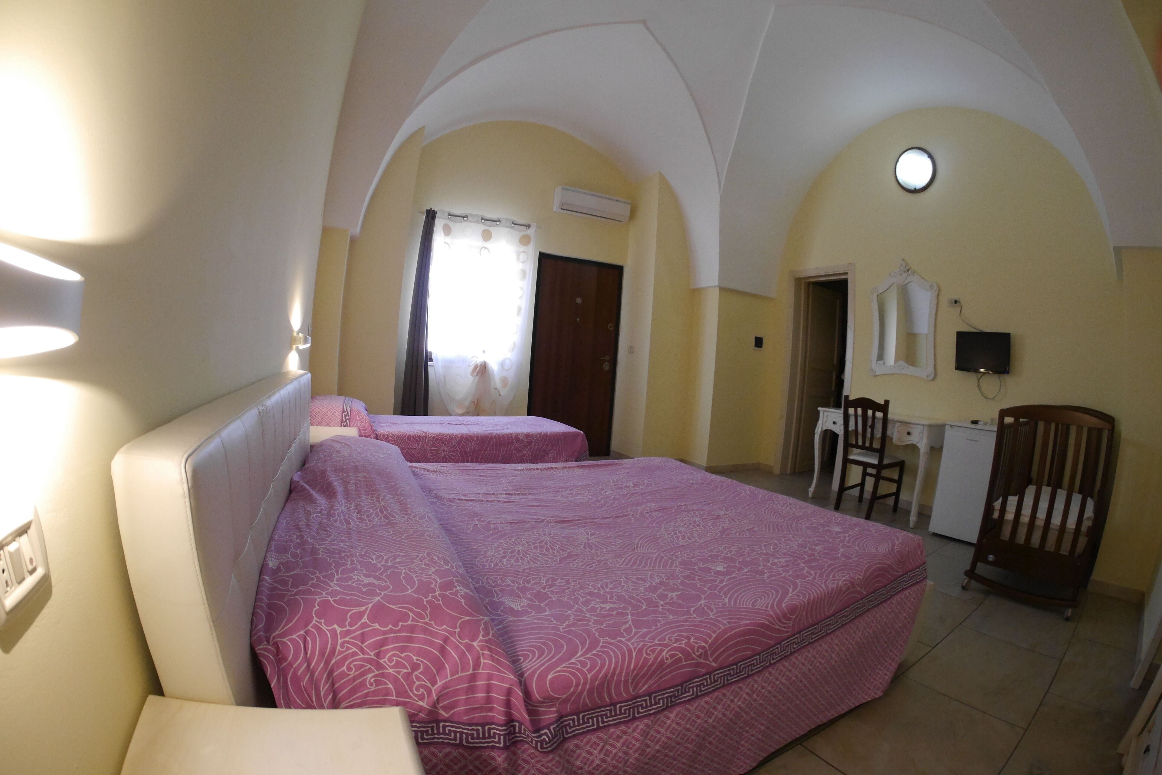 Une chambre avec deux lits, un bureau, une chaise, un berceau et un téléviseur.