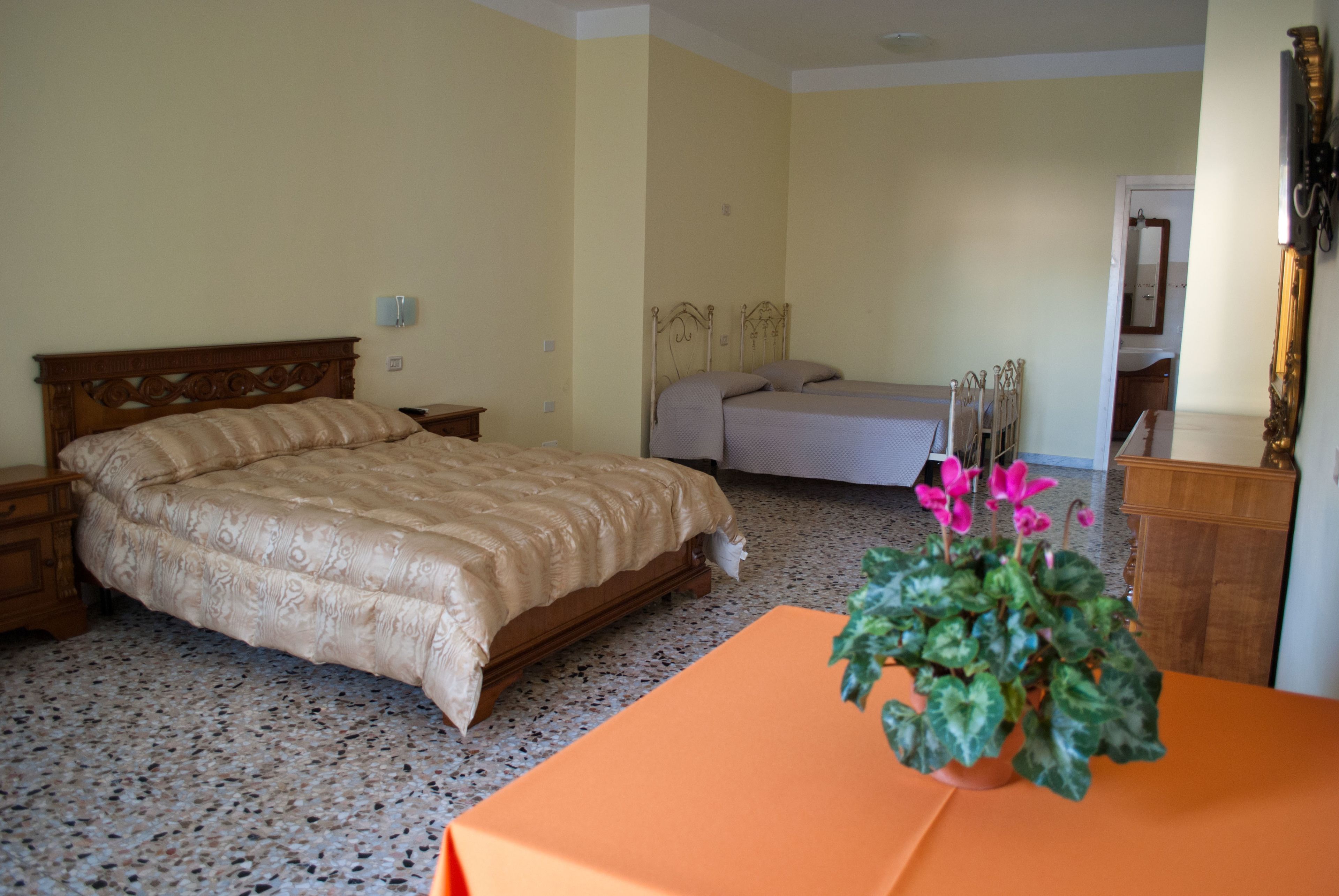 A bedroom with a large bed, a smaller bed, a nightstand, a table with a plant, and a mirror.