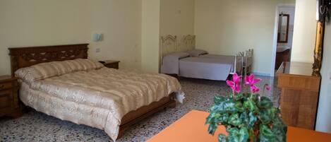 A bedroom with a large bed, a smaller bed, a nightstand, a table with a plant, and a mirror.