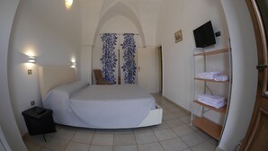 Un dormitorio con cama curva, televisor montado en la pared, estante con toallas dobladas y puerta que da a otra habitación.