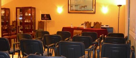 Un salón de conferencias con filas de sillas, un atril y una mesa con botellas de agua.